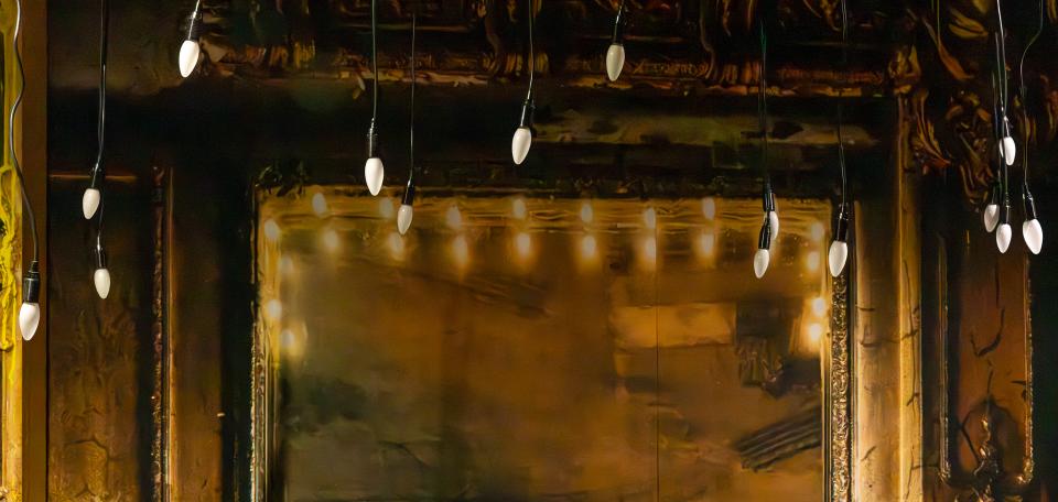 Kultainen peili, jolla kultaiset koristeelliset kehykset. Etualalla roikkuu lamppuja.