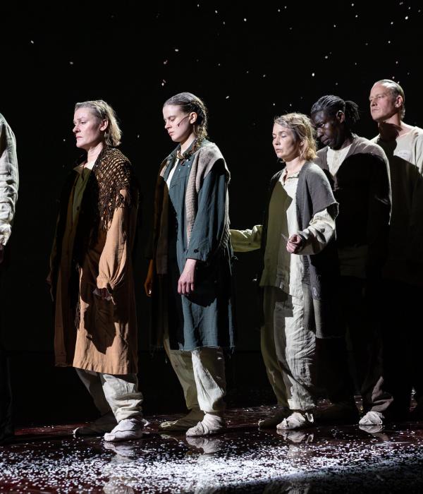 seitsemän ihmistä seisovat jonossa. heillä on uupuneet ilmeet ja kuluneet vaatteet