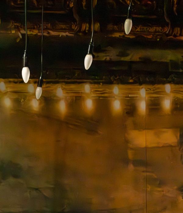 Kultainen peili, jolla kultaiset koristeelliset kehykset. Etualalla roikkuu lamppuja.