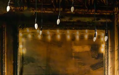 Kultainen peili, jolla kultaiset koristeelliset kehykset. Etualalla roikkuu lamppuja.