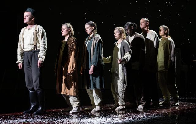 seitsemän ihmistä seisovat jonossa. heillä on uupuneet ilmeet ja kuluneet vaatteet