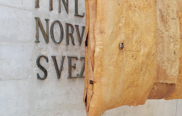 kivisellä seinällä lukee italiaksi suomi, norja ja ruotsi. maiden nimet on peitetty osittain tuohisella esineellä tai taideteoksella