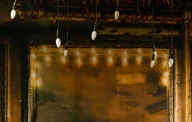 Kultainen peili, jolla kultaiset koristeelliset kehykset. Etualalla roikkuu lamppuja.